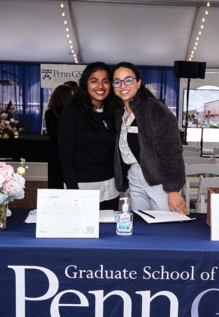 Two individuals, smiling, stand together behind a registration desk. The Penn GSE logo is seen in the background.