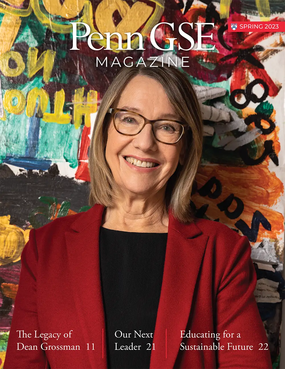 The cover of the Spring 2023 issue of The Penn GSE Magazine. A headshot of Dean Pam Grossman, who wears a red suit and brown glasses, smiling at the camera against a colorful, painted wall. The headline reads 
