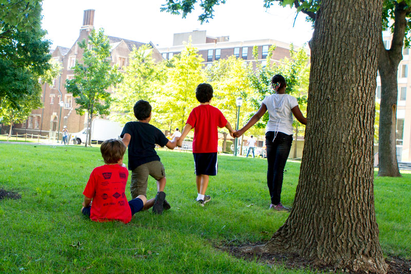 Students holding hands near a tree.